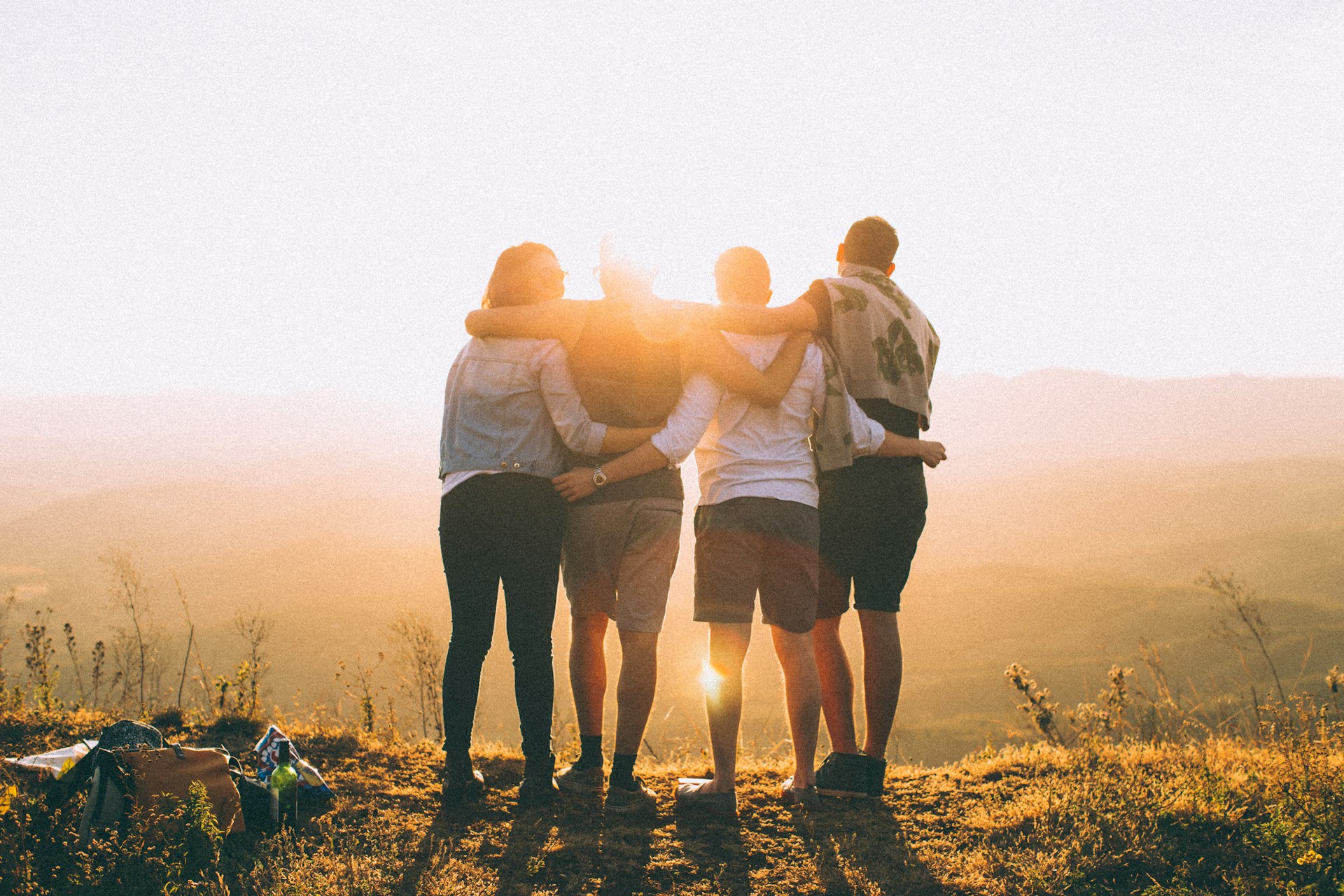 Groupe de bénévoles unis se tenant par les épaules face au coucher de soleil, illustrant l'esprit d'équipe.